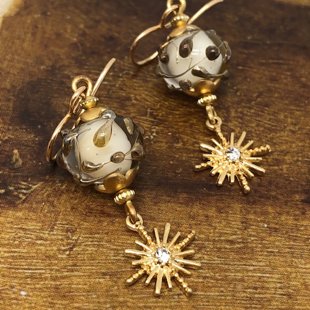Boucles d'oreilles bohème chic composées de perles en verre filé à la flamme jaune pâle et bronze et de breloques étoiles en strass doré.