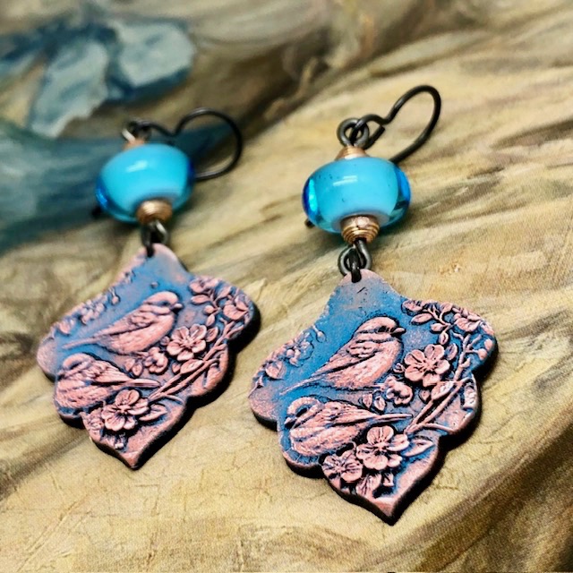 Boucles d’oreilles bohèmes composées de pendentifs en argile polymère avec un motif d'oiseau rose sur un fond bleu indigo. Bijoux uniques de créateur.