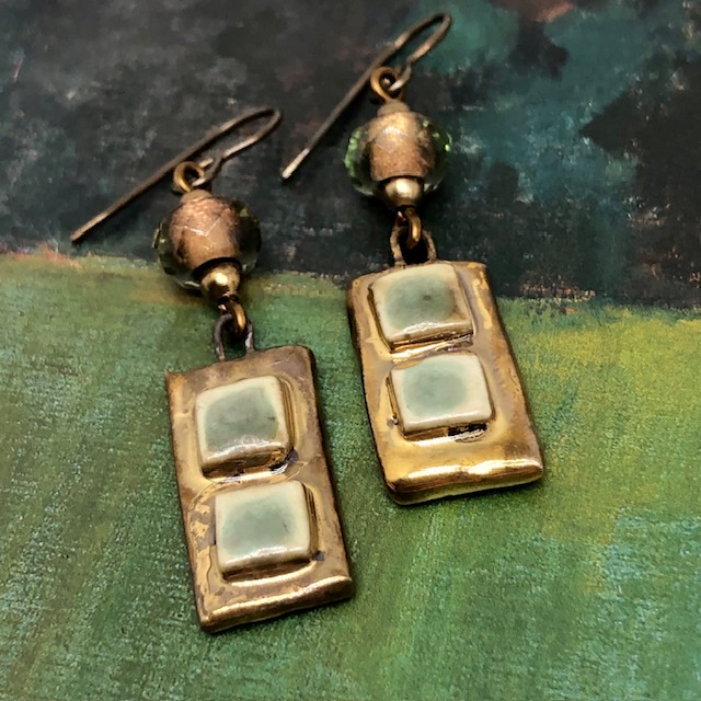 Boucles d’oreilles asymétriques composées de pendentifs artisanaux en céramique avec des carrés en relief vert amande et bronze. Bijoux uniques.