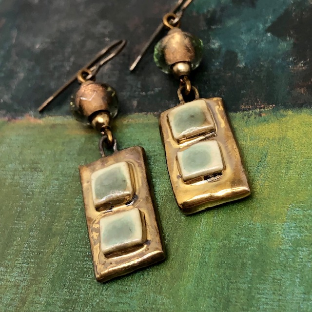Boucles d’oreilles asymétriques composées de pendentifs artisanaux en céramique avec des carrés en relief vert amande et bronze. Bijoux uniques.