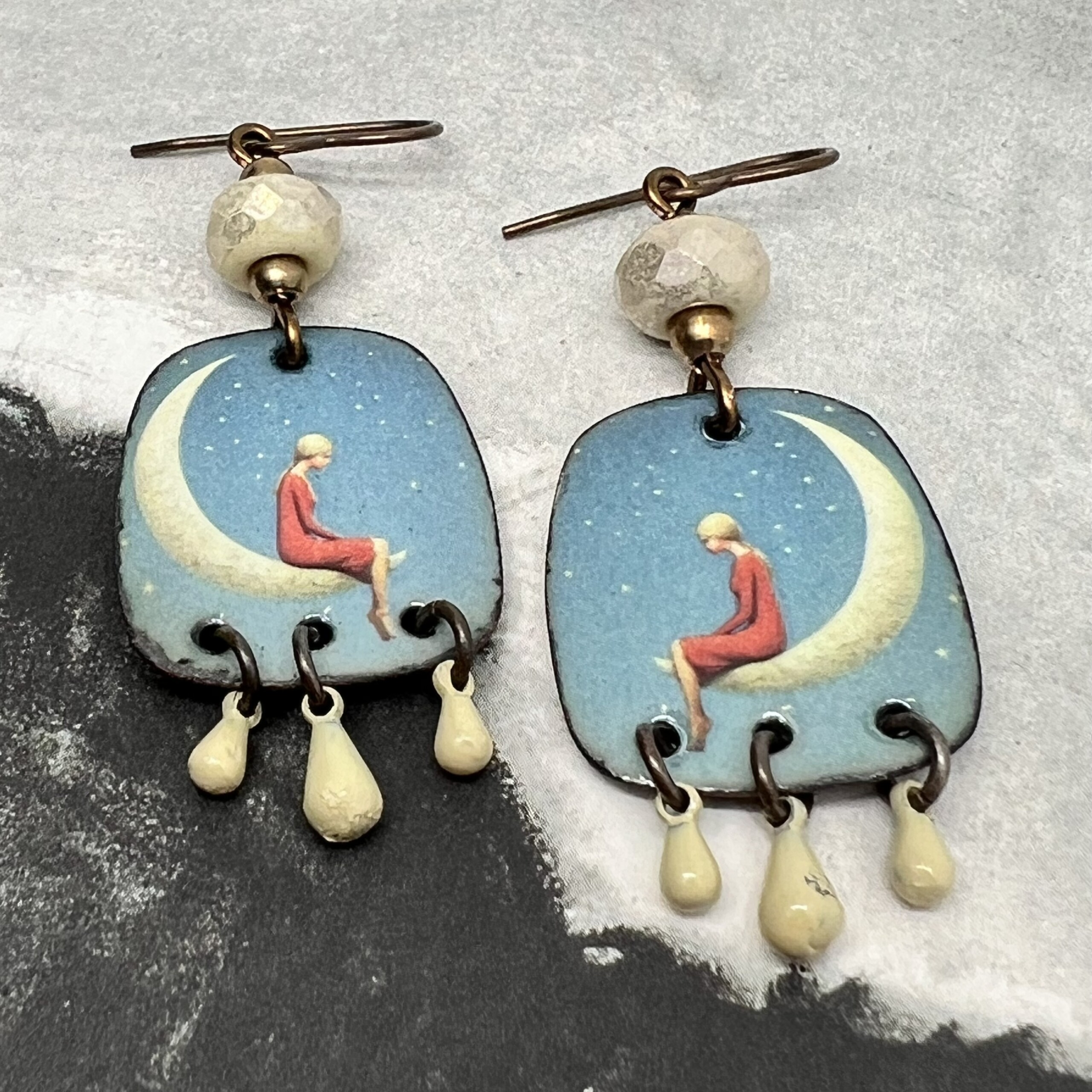 Boucles d’oreilles poétiques composées de pendentifs en cuivre émaillé avec le portrait d'une jeune fille assise sur un croissant de lune. Bijoux uniques.