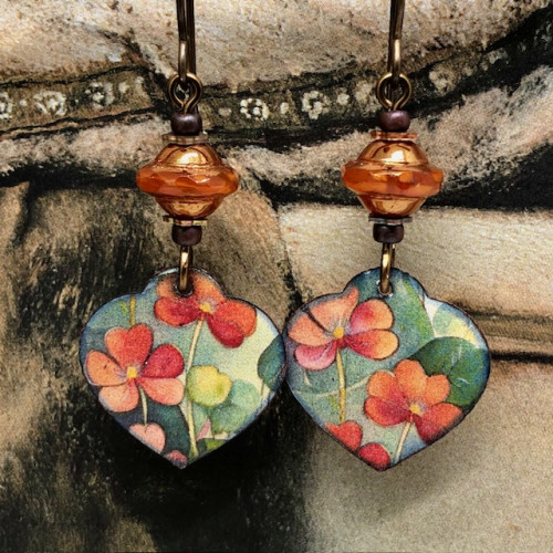 Boucles d'oreilles asymétriques bohèmes composées de pendentifs en cuivre émaillé en forme de coeur, avec un motif de fleurs orange. Bijoux uniques.