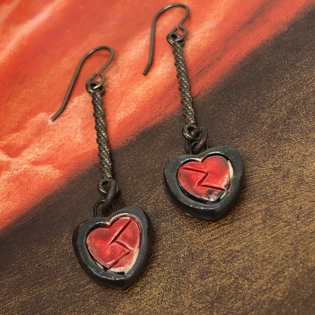 Boucles d'oreilles bohèmes composées de petits coeurs rouges en céramique et de longs connecteurs en métal noirs. Pièces uniques.