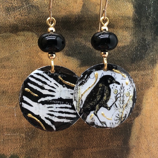 Boucles d’oreilles asymétriques composées de pendentifs en cuivre émaillé représentant deux mains de squelette et un corbeau. Bijoux uniques.