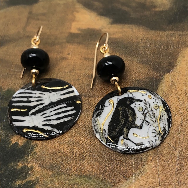 Boucles d’oreilles asymétriques composées de pendentifs en cuivre émaillé représentant deux mains de squelette et un corbeau. Bijoux uniques.