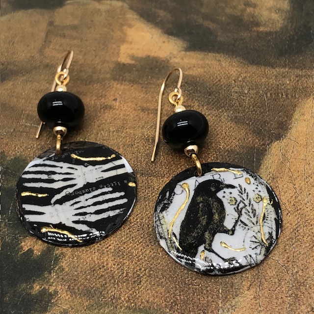 Boucles d’oreilles asymétriques composées de pendentifs en cuivre émaillé représentant deux mains de squelette et un corbeau. Bijoux uniques.