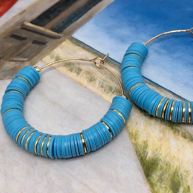 Boucles d'oreilles créoles composées de perles africaines Heishi en vinyles recyclés bleu ciel et de perles en laiton dorées à l'or fin.