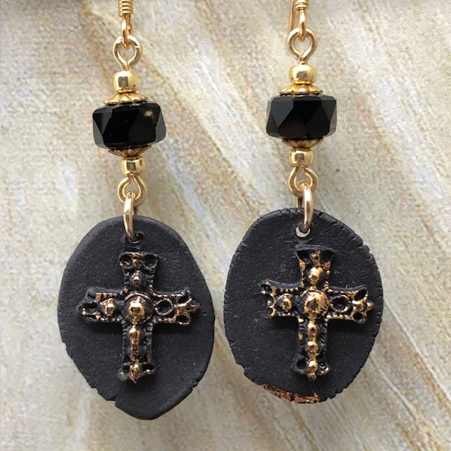 Boucles d'oreilles baroques composées de pendentifs en céramique avec une croix dorée en relief sur un fond noir mat. Bijoux uniques.