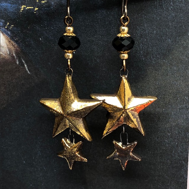 Boucles d'oreilles bohèmes composées de pendentifs en céramique en forme d'étoiles dorées et de perles en cristal Swarovski noires. Bijoux uniques.