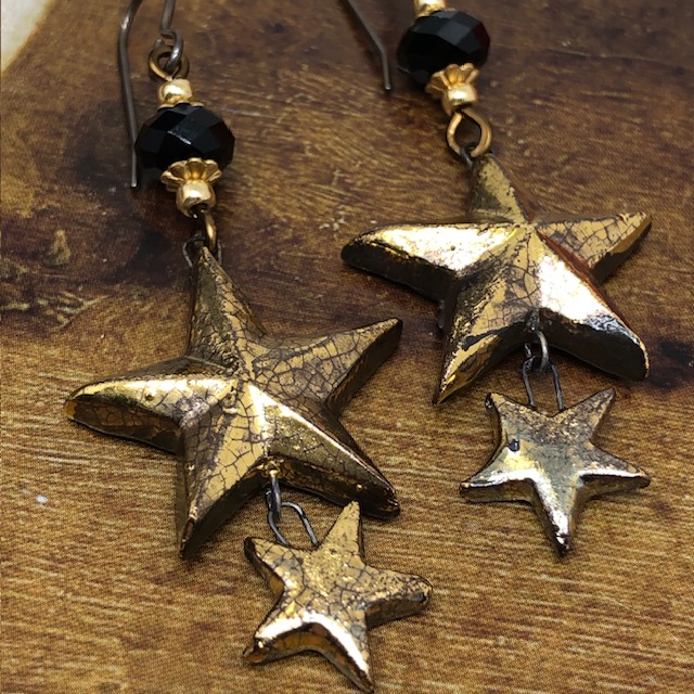 Boucles d'oreilles bohèmes composées de pendentifs en céramique en forme d'étoiles dorées et de perles en cristal Swarovski noires. Bijoux uniques.