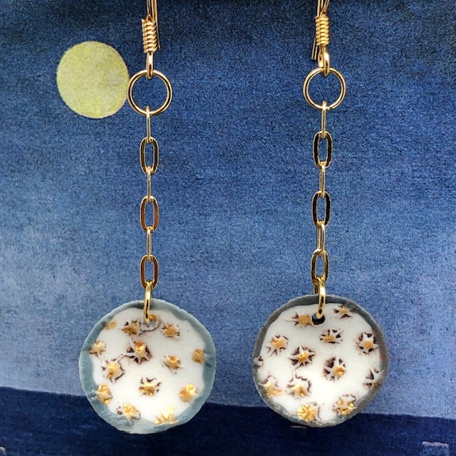 Petites boucles d'oreilles de créateur composées de pendentifs en porcelaine ronds, avec de petites étoiles dorées sur un fond blanc. Bijoux uniques.