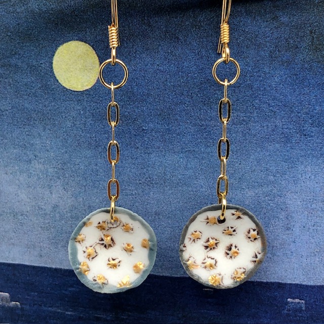 Petites boucles d'oreilles de créateur composées de pendentifs en porcelaine ronds, avec de petites étoiles dorées sur un fond blanc. Bijoux uniques.