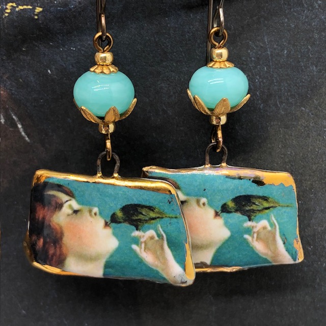 Boucles d'oreilles de créateur composées de pendentifs en céramique représentant un oiseau picorant sur les lèvres d'une jeune femme. Bijoux uniques.