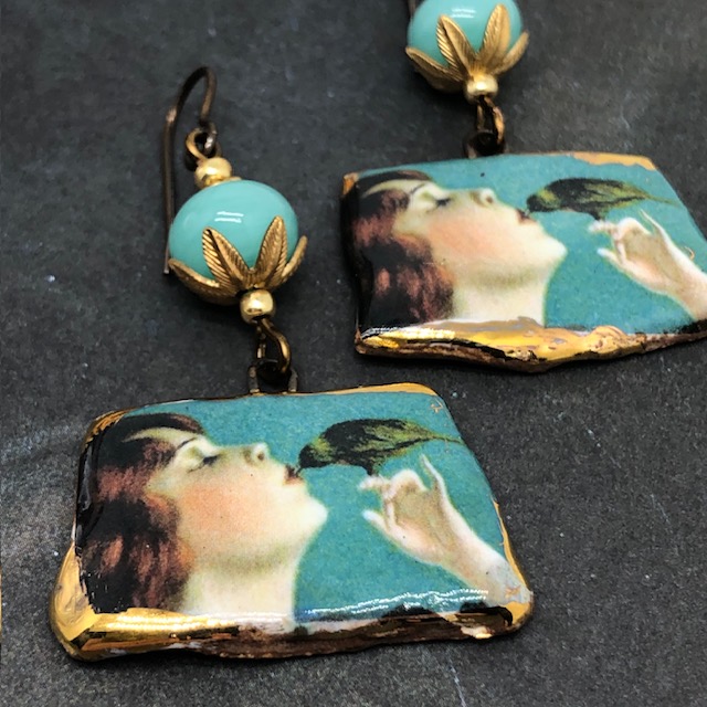 Boucles d'oreilles de créateur composées de pendentifs en céramique représentant un oiseau picorant sur les lèvres d'une jeune femme. Bijoux uniques.
