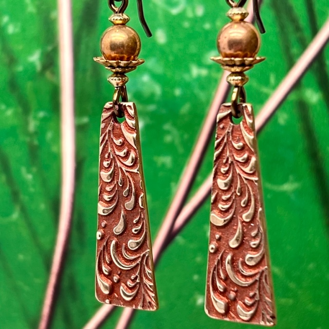 Boucles d'oreilles bohèmes composées de pendentifs en bronze avec un motif de feuillage doré sur un fond rouge brique. Bijoux uniques.