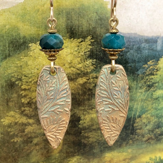Boucles d'oreilles bohème composées de pendentifs artisanaux en bronze avec un motif de feuillage et de perles facettées en apatite de couleur émeraude.