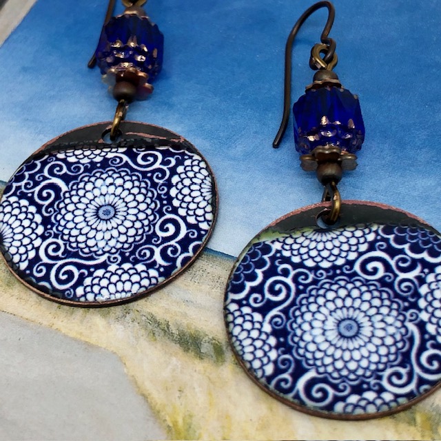 Boucles d'oreilles bohèmes composées de pendentifs en cuivre émaillé représentant des dahlias bancs sur un fond bleu marine. Modèle unique.