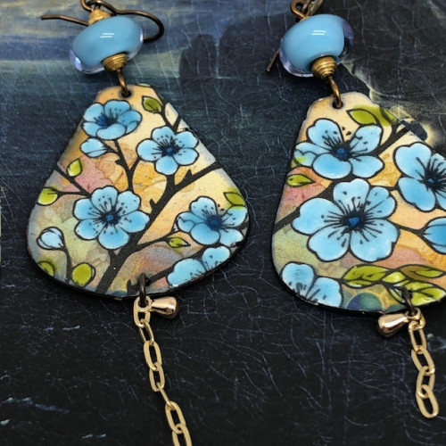 Boucles d'oreilles bohèmes asymétriques composées de pendentifs en cuivre émaillé avec un motif de fleurs bleues et safran. Modèles uniques.