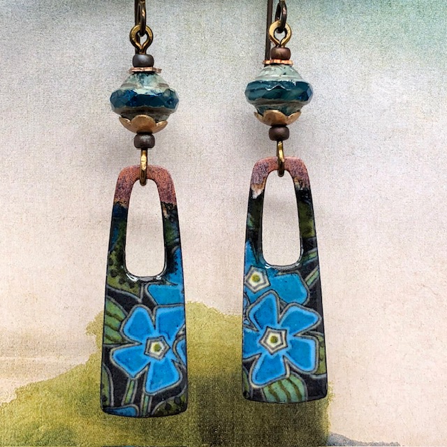 Boucles d’oreilles bohèmes composées de pendentifs en cuivre émaillé représentant des fleurs bleues sur un fond de feuilles vertes. Bijoux uniques.