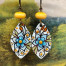 Boucles d'oreilles bohèmes asymétriques composées de pendentifs en cuivre émaillé avec un motif de fleurs bleues et safran. Modèles uniques.