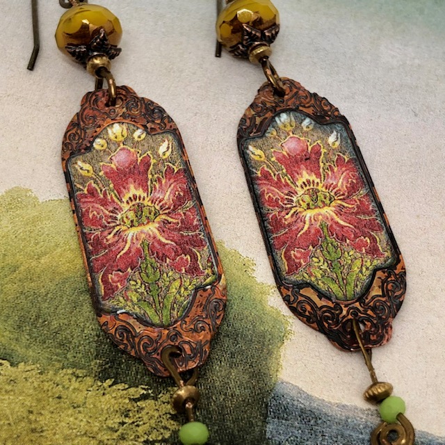 Boucles d'oreilles bohèmes composées de pendentifs en cuivre émaillé représentant des fleurs sauvages rouge et jaune sur un fond vert. Pièces uniques.