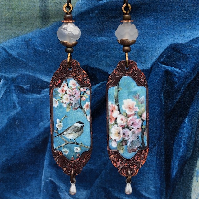Boucles d'oreilles bohèmes asymétriques composées de pendentifs en cuivre émaillé représentant un oiseau et une branche de cerisiers. Bijoux uniques.