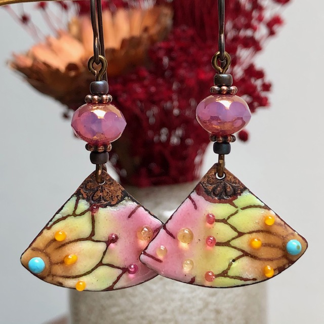 Boucles d’oreilles asymétriques bohème chic composées de pendentifs artisanaux en cuivre émaillé au motif abstrait et multicolore.