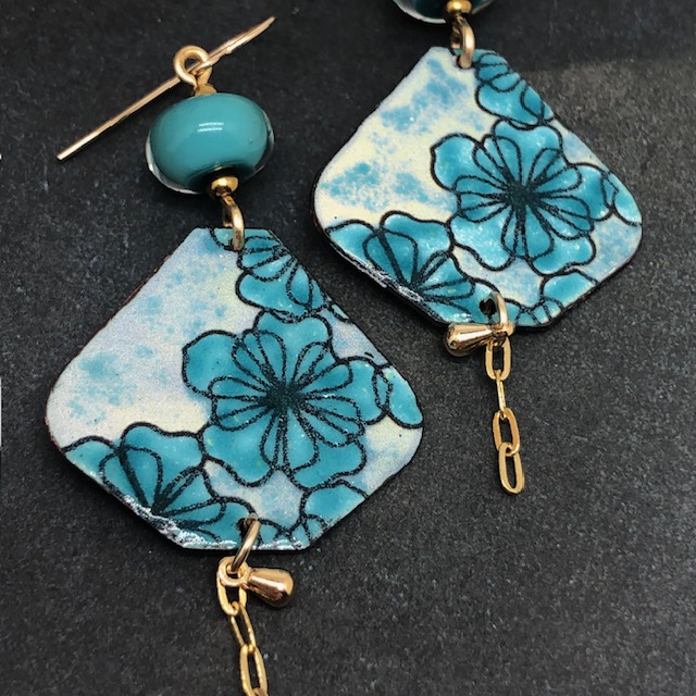 Grandes boucles d'oreilles bohèmes asymétriques composées de pendentifs en cuivre émaillé avec un motif de fleurs bleues turquoise. Bijoux uniques.