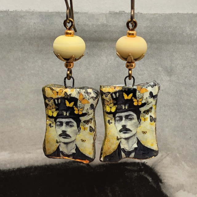 Boucles d’oreilles bohèmes asymétriques composées de pendentifs en céramique avec le portrait d'un homme entourée de papillons. Bijoux uniques.