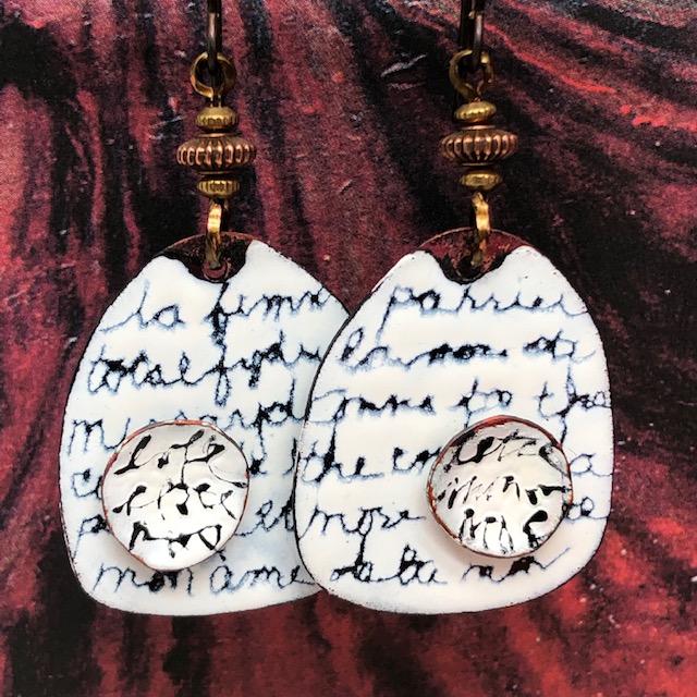 Boucles d'oreilles bohèmes composées de pendentifs en cuivre émaillé noir et blanc, avec un texte en français et un autre en anglais. Pièces uniques.