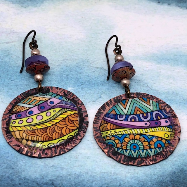 Boucles d'oreilles vintage composées de pendentifs artisanaux ronds multicolore en cuivre émaillé, de perles en verre tchèque lilas.