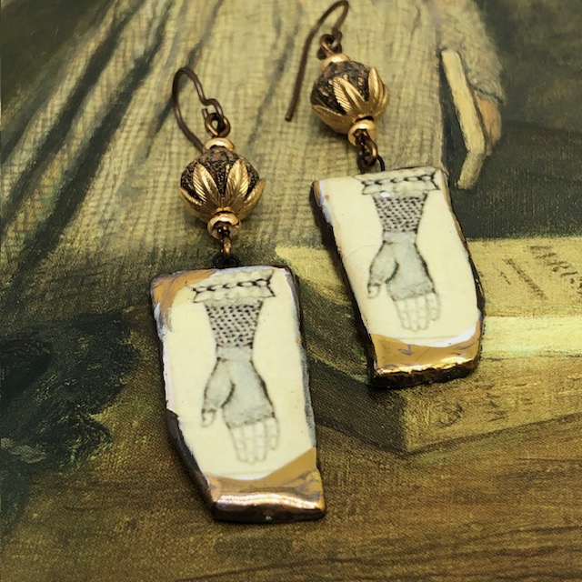 Boucles d’oreilles asymétriques composées de pendentifs en céramique représentant une main avec une mitaine en dentelle couleur sépia. Bijoux uniques.