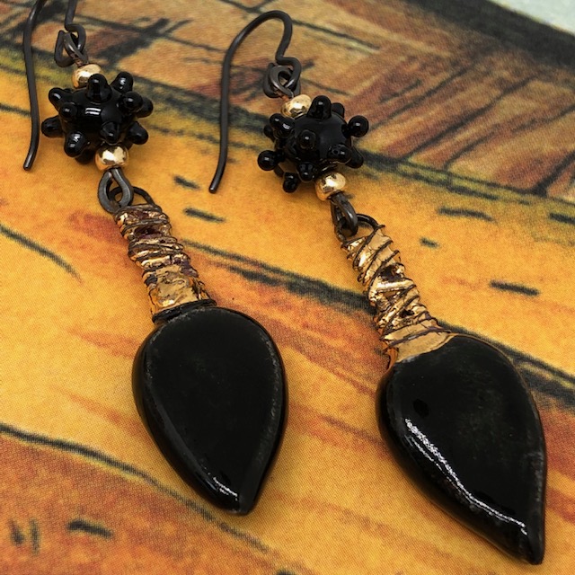 Boucles d'oreilles bohème chic composées de pendentifs en céramique noir et or et de perles en verre filé à la flamme noires. Pièces uniques.