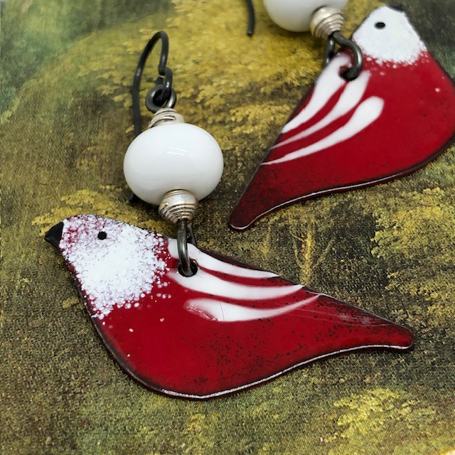 Boucles d'oreilles bohèmes composées de pendentifs en cuivre émaillé représentant un oiseau rouge aux ailes blanches. Modèle unique.