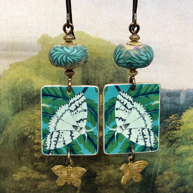 Boucles d'oreilles de créateur bohèmes en cuivre illustré et pâte polymère représentant des papillons blancs sur un feuillage.