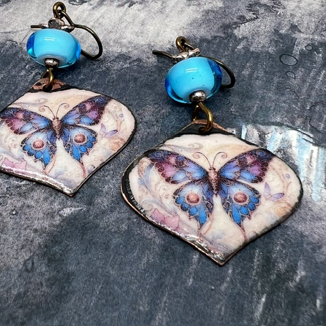 Boucles d'oreilles bohèmes composées de pendentifs en cuivre émaillé avec un papillon bleu et mauve. Bijoux uniques de créateur.