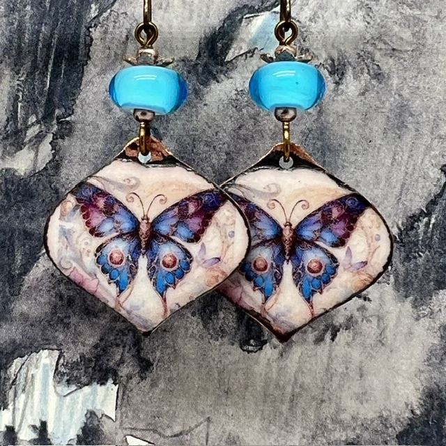 Boucles d'oreilles bohèmes composées de pendentifs en cuivre émaillé avec un papillon bleu et mauve. Bijoux uniques de créateur.