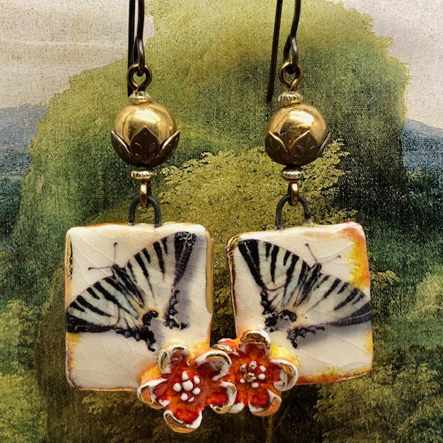 Boucles d'oreilles bohèmes composées de pendentifs artisanaux représentant un papillon noir et une fleur orange. Bijoux uniques.