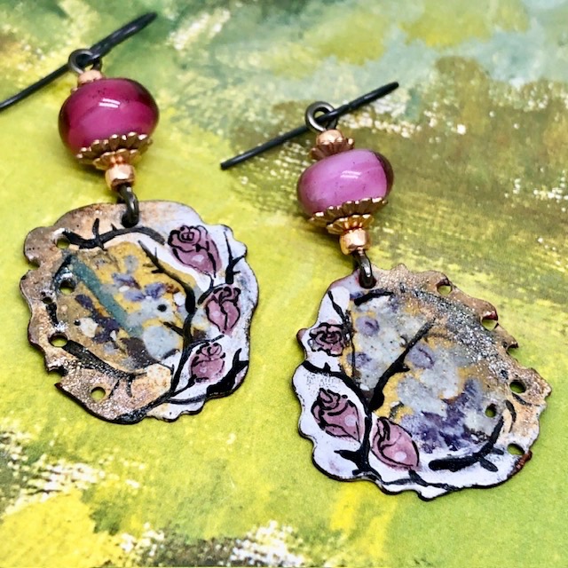 Boucles d’oreilles bohèmes asymétriques composées de pendentifs en cuivre émaillé avec un motif de rose sur un fond or. Bijoux uniques de créateur.