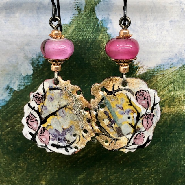 Boucles d’oreilles bohèmes asymétriques composées de pendentifs en cuivre émaillé avec un motif de rose sur un fond or. Bijoux uniques de créateur.