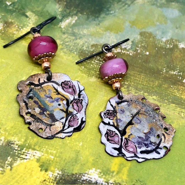 Boucles d’oreilles bohèmes asymétriques composées de pendentifs en cuivre émaillé avec un motif de rose sur un fond or. Bijoux uniques de créateur.