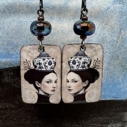 Boucles d'oreilles uniques composées de pendentifs en cuivre émaillé avec le portrait d'une femme portant une tasse en guise de chapeau.