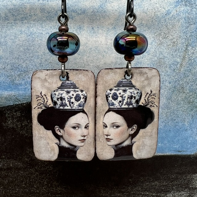 Boucles d'oreilles uniques composées de pendentifs en cuivre émaillé avec le portrait d'une femme portant une tasse en guise de chapeau.