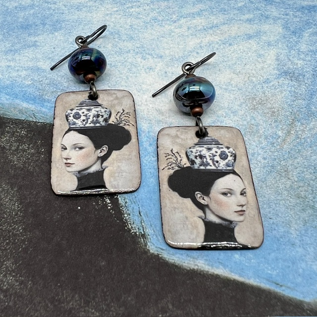 Boucles d'oreilles uniques composées de pendentifs en cuivre émaillé avec le portrait d'une femme portant une tasse en guise de chapeau.