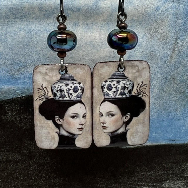 Boucles d'oreilles uniques composées de pendentifs en cuivre émaillé avec le portrait d'une femme portant une tasse en guise de chapeau.