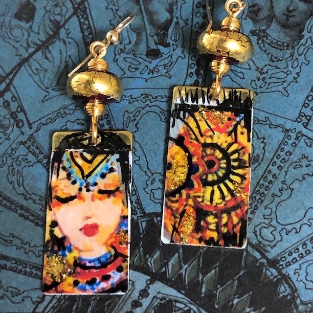 Boucles d'oreilles asymétriques composées de pendentifs en laiton émaillé, avec le visage d'une princesse hindoue et un mandala. Bijoux uniques.