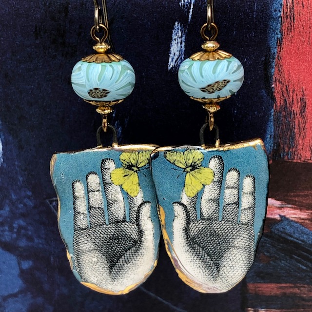 Boucles d'oreilles artisanales bohème composées de pendentifs en céramique bleus et jaunes représentant un papillon sur une main.en c
