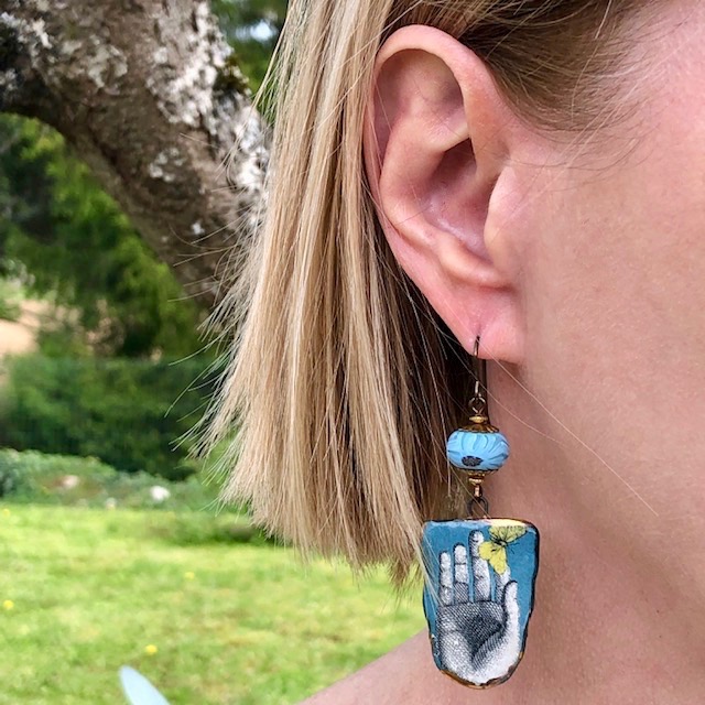 Boucles d'oreilles artisanales bohème composées de pendentifs en céramique bleus et jaunes représentant un papillon sur une main.en c