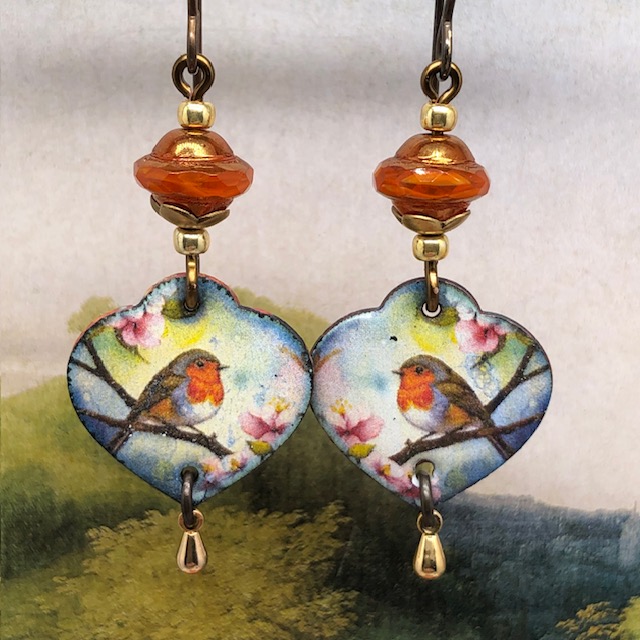 Boucles d’oreilles poétiques composées de pendentifs en cuivre émaillé en forme de coeur avec un rouge-gorge sur un fond multicolore. Bijoux uniques.