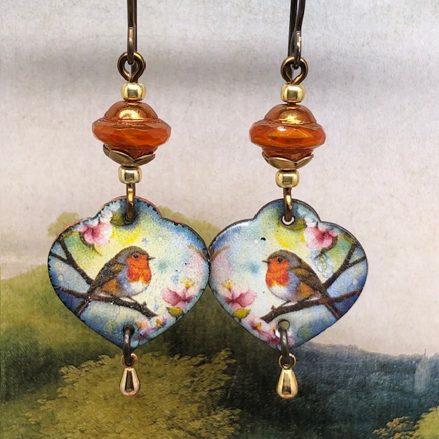 Boucles d’oreilles poétiques composées de pendentifs en cuivre émaillé en forme de coeur avec un rouge-gorge sur un fond multicolore. Bijoux uniques.